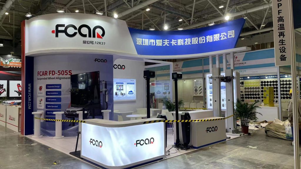 Trade show booth featuring a car and wheel alignment system display in a bustling convention hall.