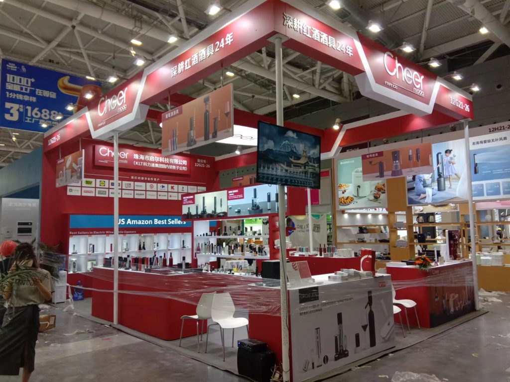 A red and white exhibition booth displaying numerous wine accessories, with workers preparing for an event.