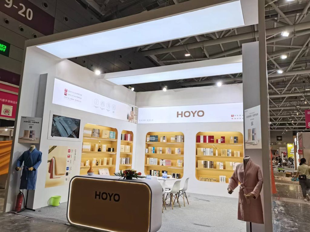 Exhibition booth featuring shelves filled with packaged products, a main counter, a display screen, and two mannequins in robes.