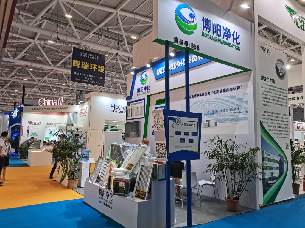Trade show booth featuring various air purification filters and equipment displays. Attendees browse, surrounded by other exhibits.
