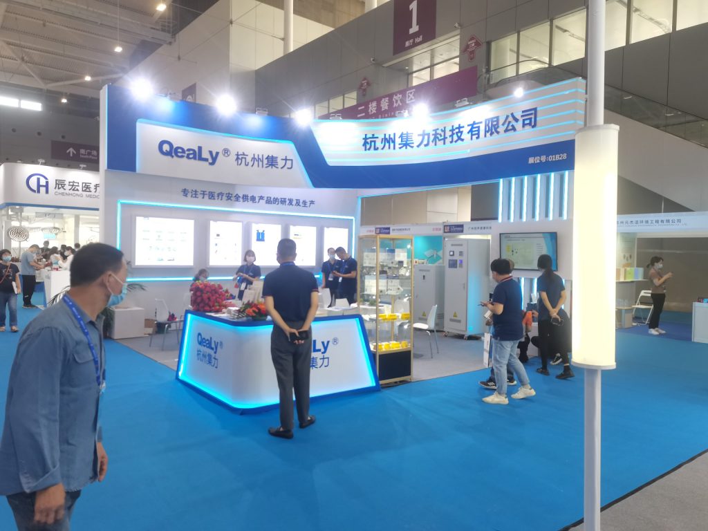 Wide shot of a trade show booth in a large hall, with visitors.