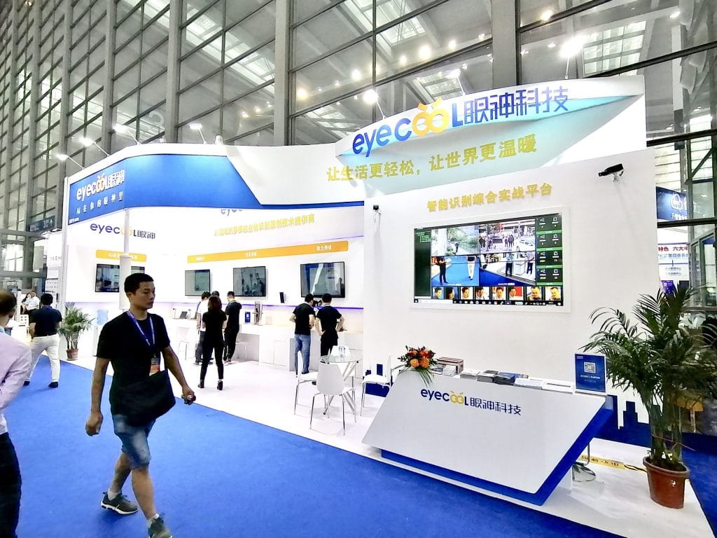 People at a white and blue tech booth in a convention hall.