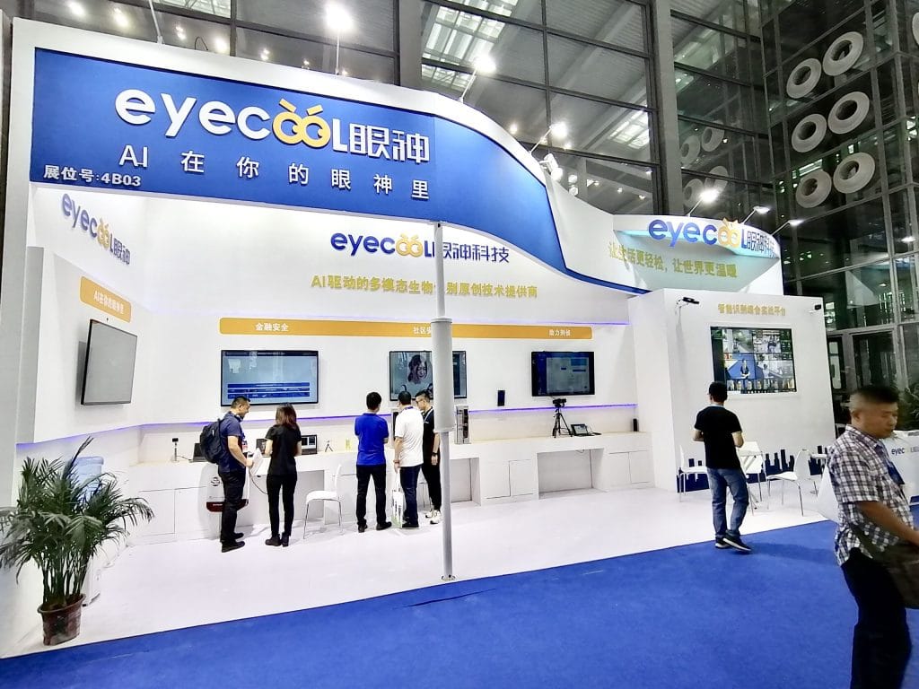 Attendees view screens at a white and blue tech booth.