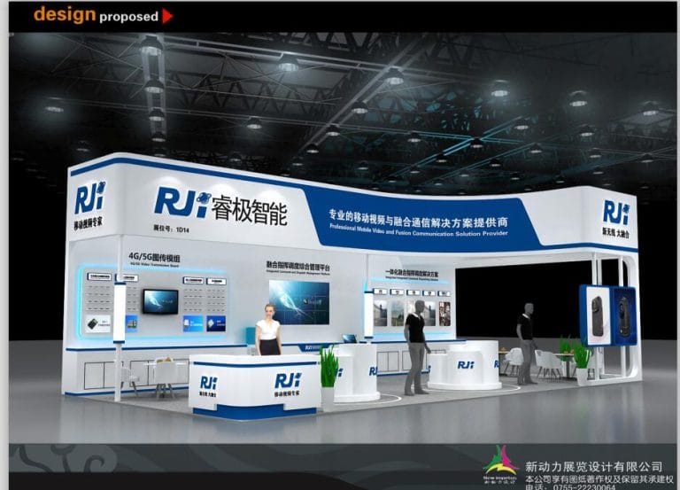 Digital rendering of a modern white and blue exhibition booth. The design features multiple screens, counters, and figures, with a seating area.
