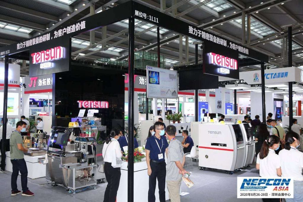 A busy exhibition hall filled with masked visitors and active booths showcasing machinery and technology.