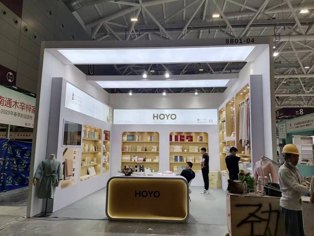 An exhibition booth under construction in a large hall, featuring display shelves, a counter, and people working.