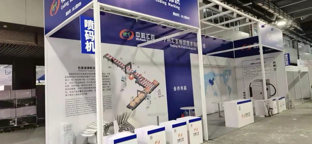 A trade show booth with a packaging line diagram, world map, and Chinese text displays.