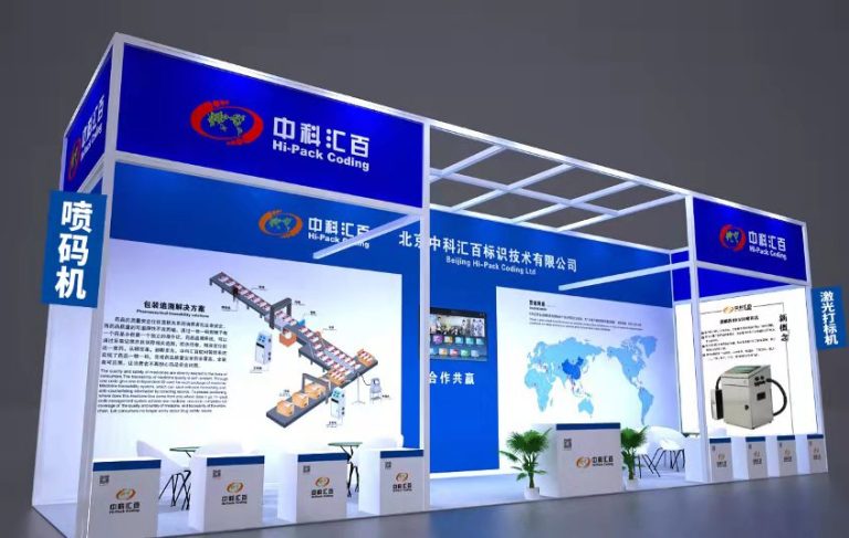 A brightly lit exhibition booth with packaging line diagrams, a world map, and a marking machine.