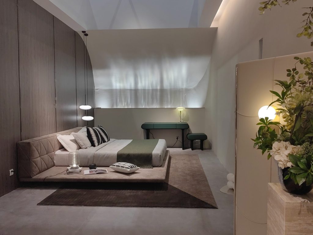 Modern bedroom with a large low platform bed, dark green console table and stool, and white walls with ambient lighting.