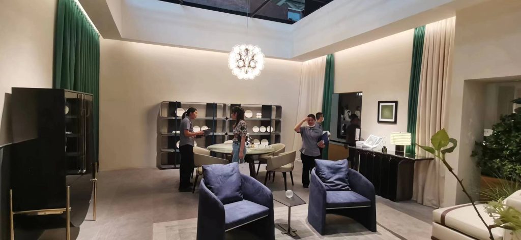 Modern dining and lounge area with two blue velvet armchairs, a round dining table with people, and a spherical chandelier.