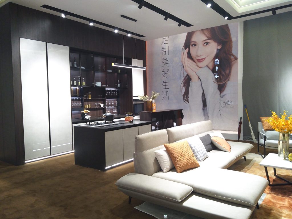Modern kitchen and living area with a grey sectional sofa, dark island, and a large wall mural of a woman.