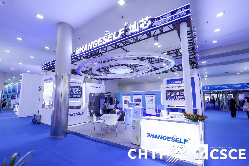 A modern exhibition booth with blue and white lighting and interactive displays is set within a large expo hall.