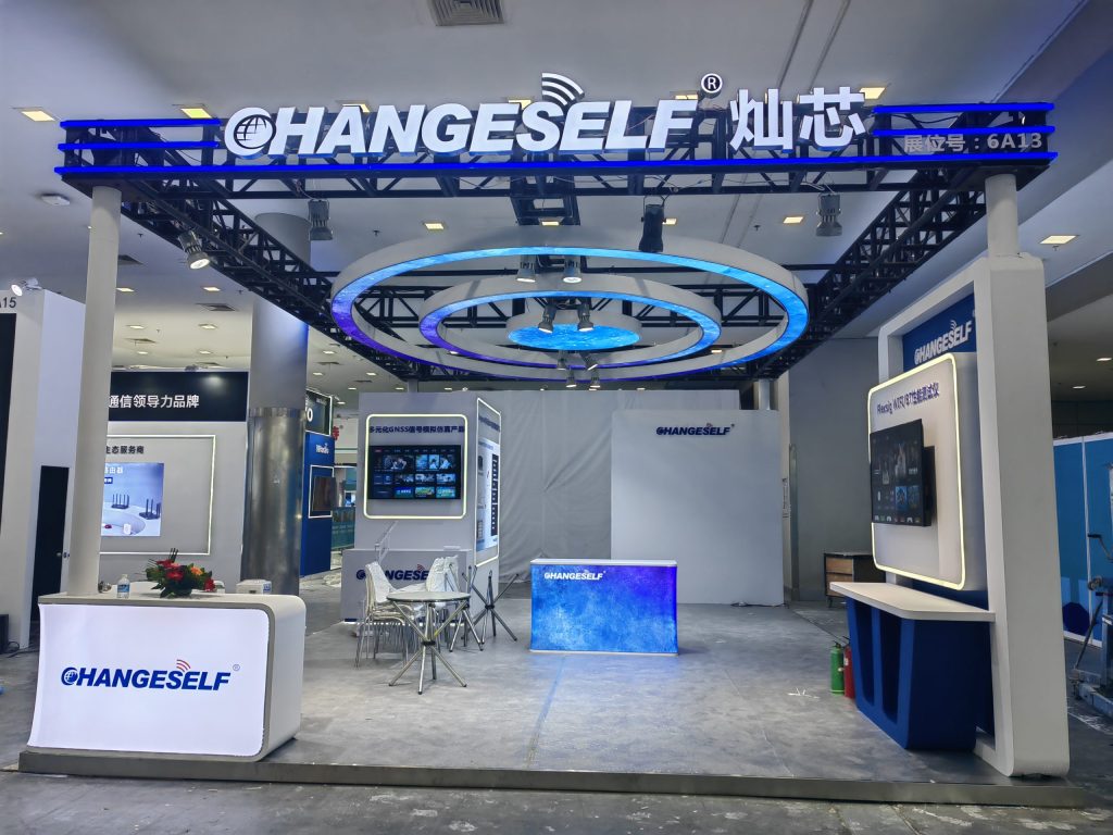 An empty exhibition booth features blue illuminated signage, display screens, and a small seating area, likely before or after an event.