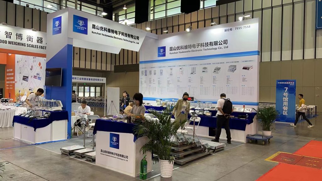Busy blue and white exhibition booth with multiple people browsing product displays and interacting.