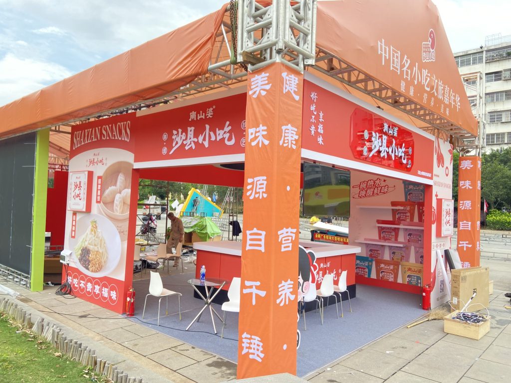 Exterior view of a red food stall with promotional banners and images of food products in an outdoor setting.