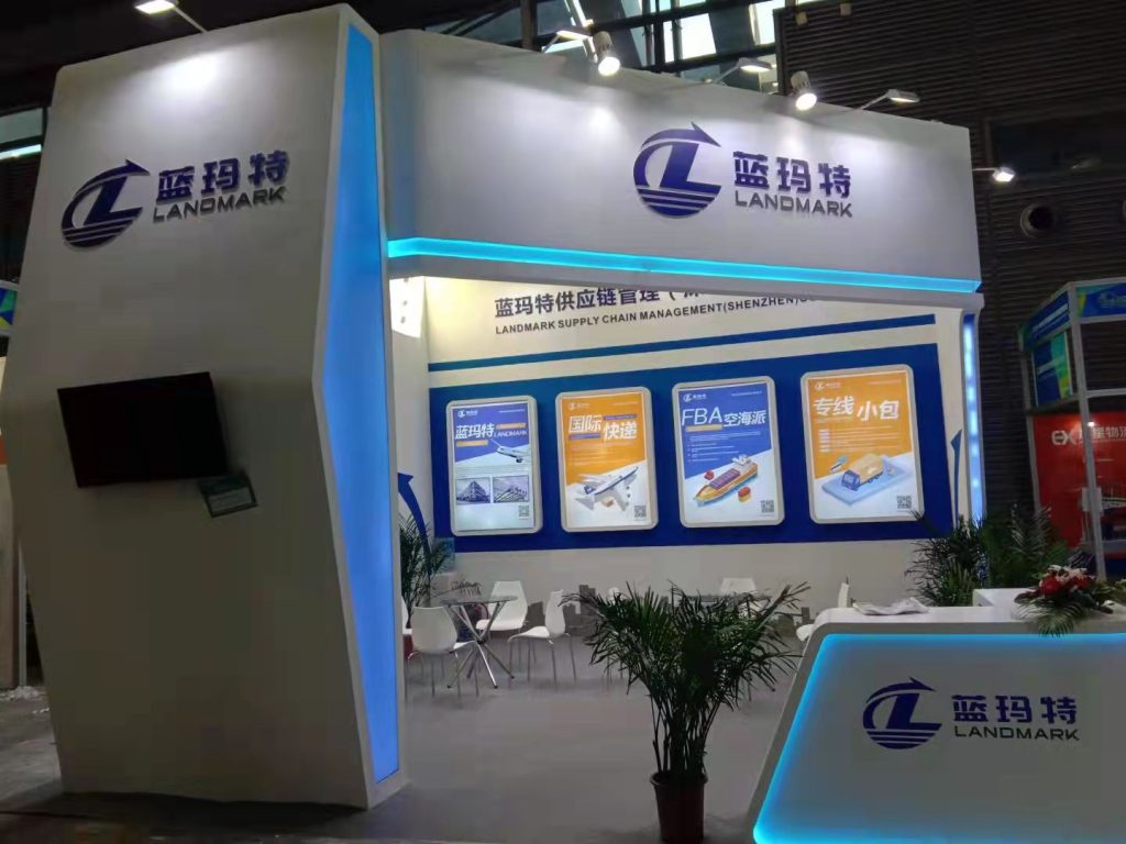 A white and blue exhibition booth featuring a glowing reception desk and four large display panels.
