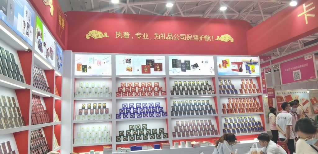 A wall of a red exhibition booth featuring shelves neatly filled with numerous small, colorful packaged products. Gold cloud decorations are at the top.