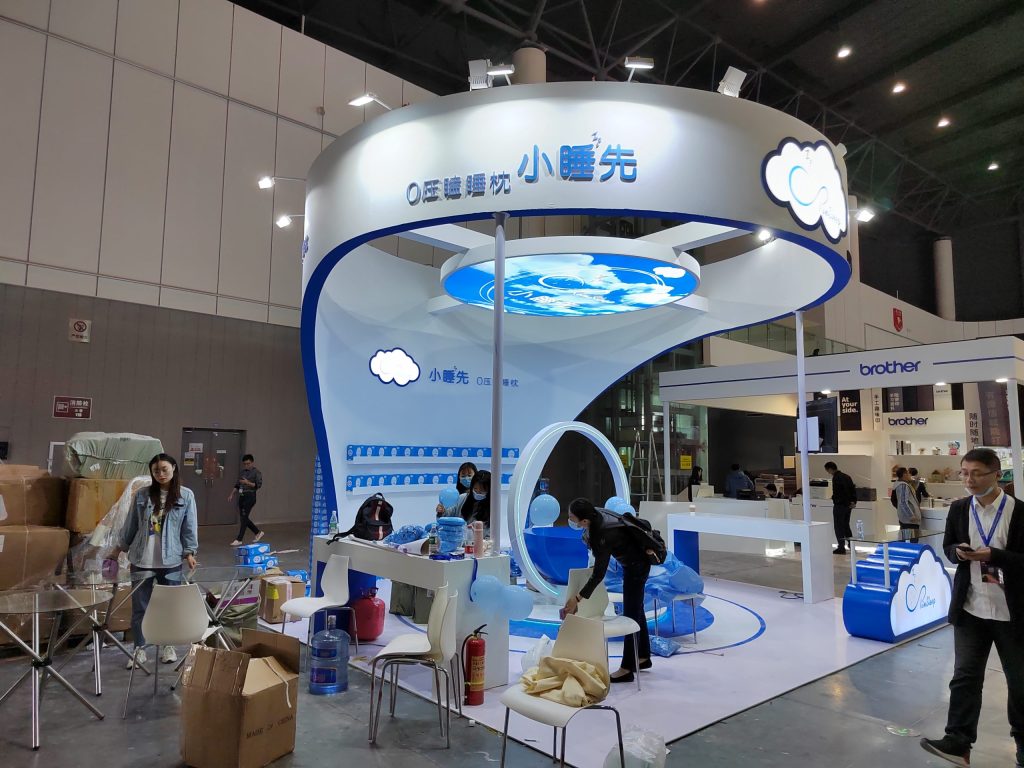 People set up a white and blue trade show booth with a cloud design, surrounded by boxes and supplies.