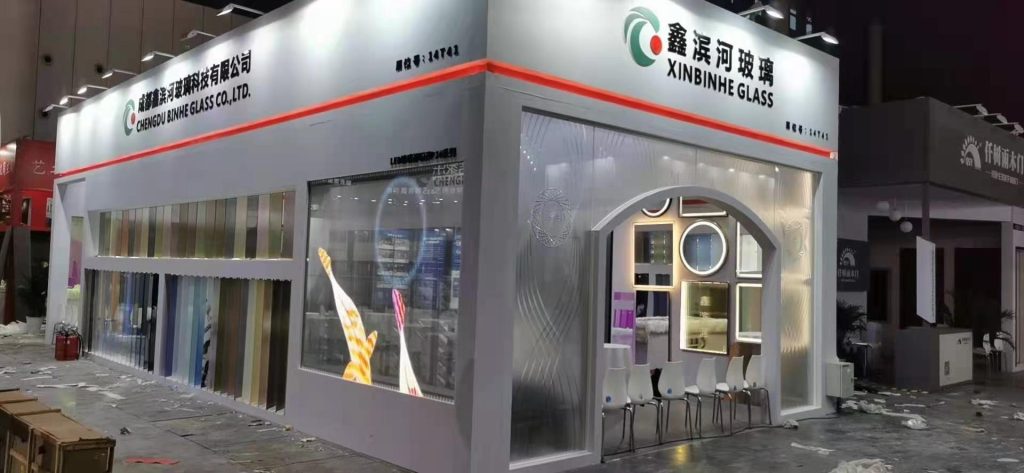 Exhibition booth with a display of colored glass panels, a transparent screen showing a glowing hand, and an arched entrance with decorative framed mirrors.
