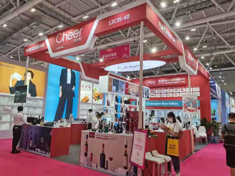 A vibrant red and white trade show booth with displayed products and large screens, with attendees browsing the exhibits in a busy hall.