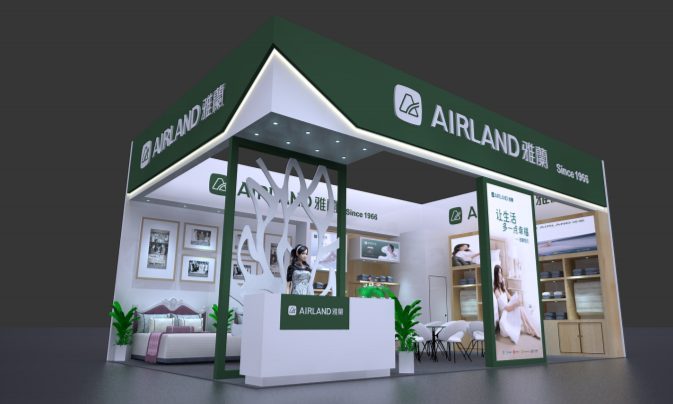 3D render of a modern trade show booth with green and white elements. It features a bed, bedding displays, and a reception desk.