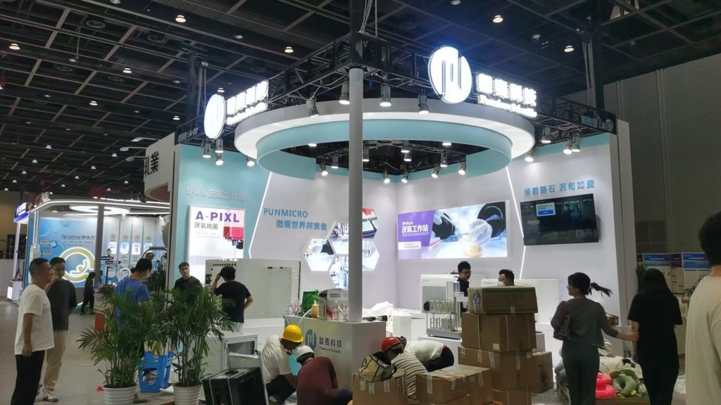 Workers arranging boxes and equipment at an exhibition booth.