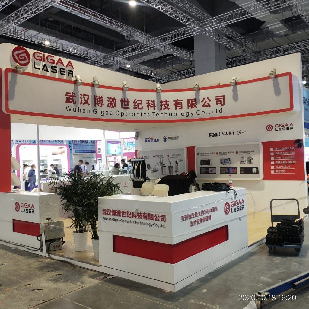 A white and red exhibition booth with product displays, potted plants, and equipment on a concrete floor.