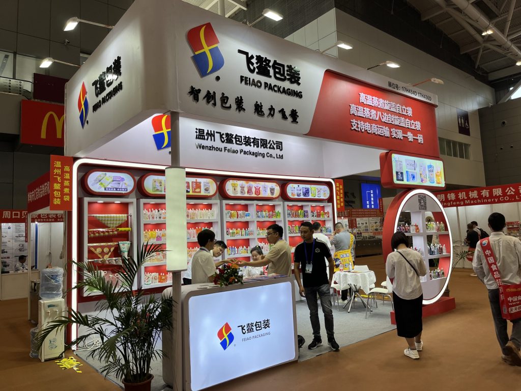 Busy trade show booth featuring red walls, product displays, and a counter with staff interacting with attendees.