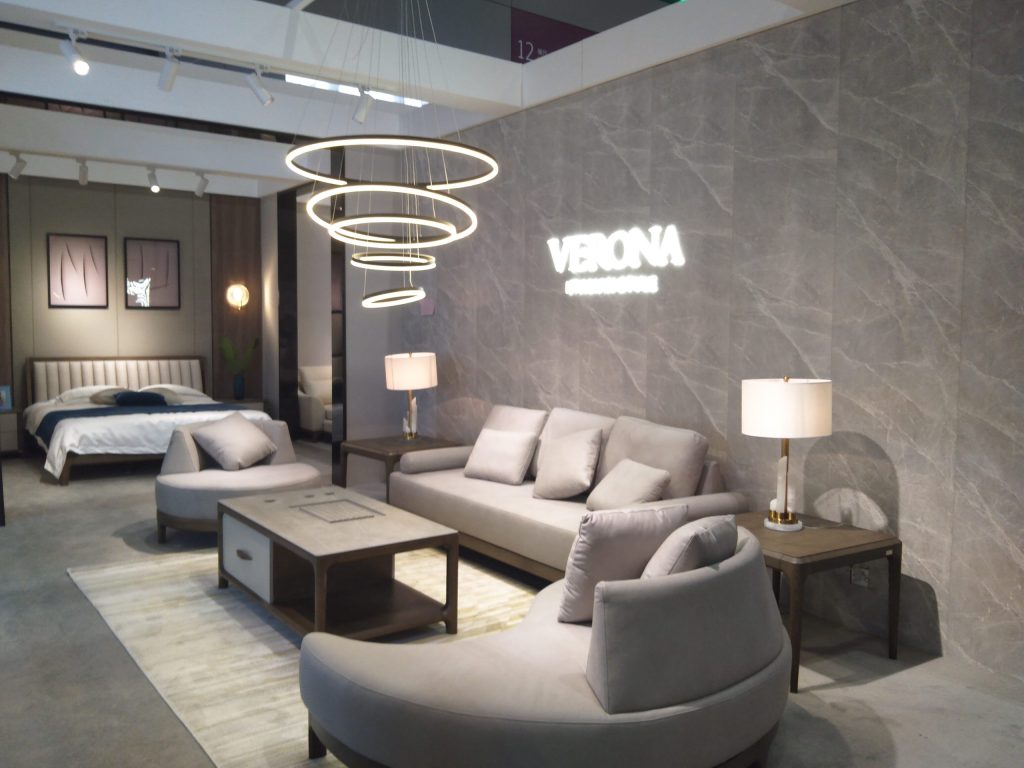 Elegant living and bedroom display with two light grey sofas, a coffee table, a bed, and circular hanging lights.