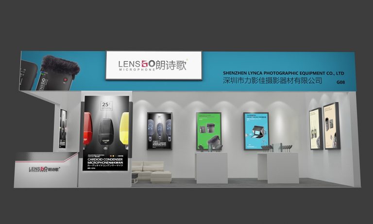 Frontal view of a clean exhibition booth featuring white display tables with microphones and large framed product posters, alongside a small white sofa.