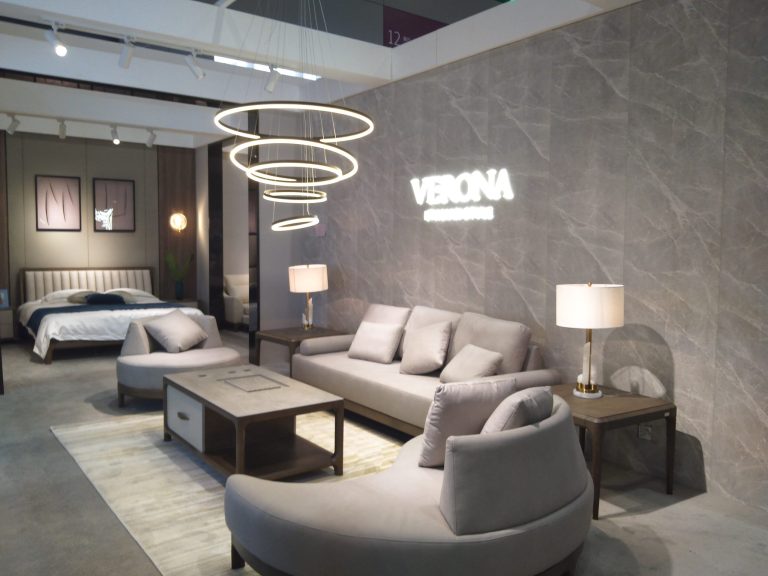 Elegant living and bedroom display with two light grey sofas, a coffee table, a bed, and circular hanging lights.