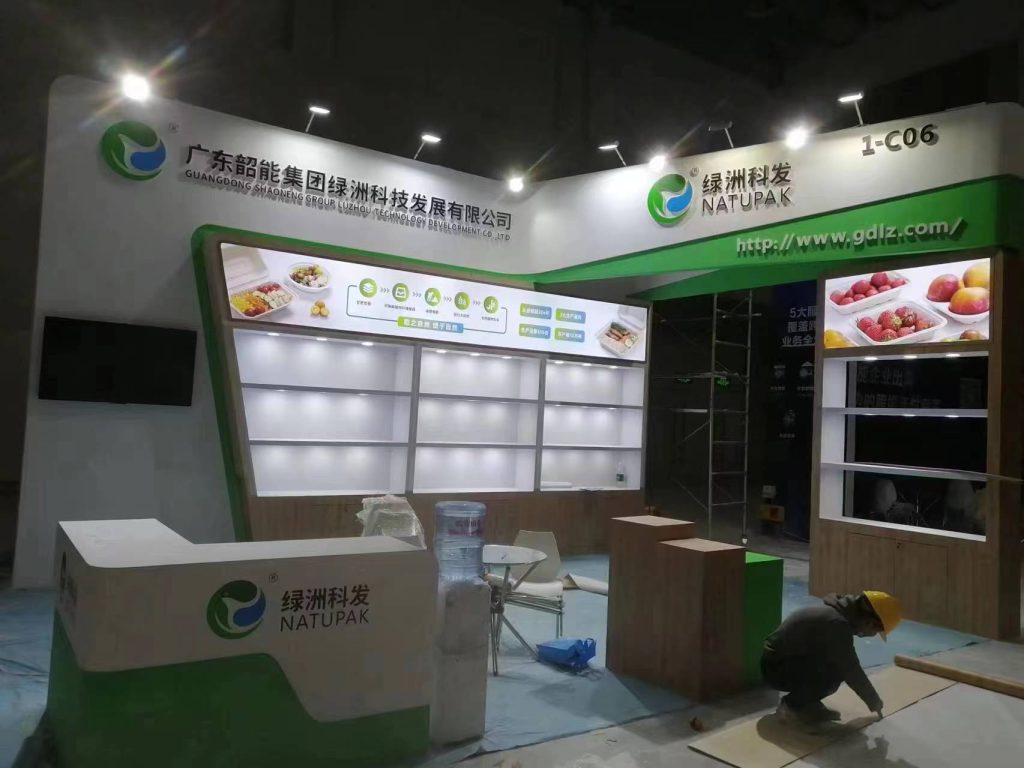 Worker on floor assembling a white and green trade show booth with display shelves and images of food.