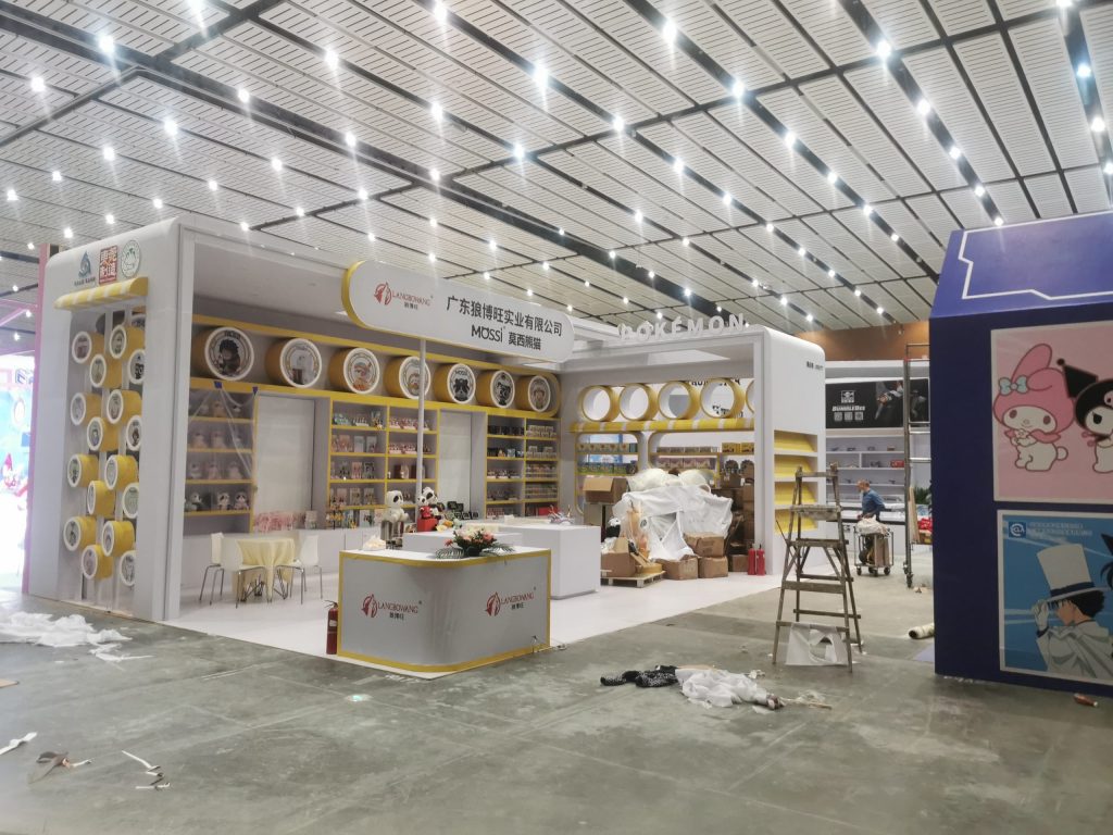 Brightly lit white and yellow exhibition booth with shelves of products and a counter.