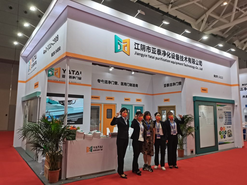 Five masked women pose at a white exhibition booth.
