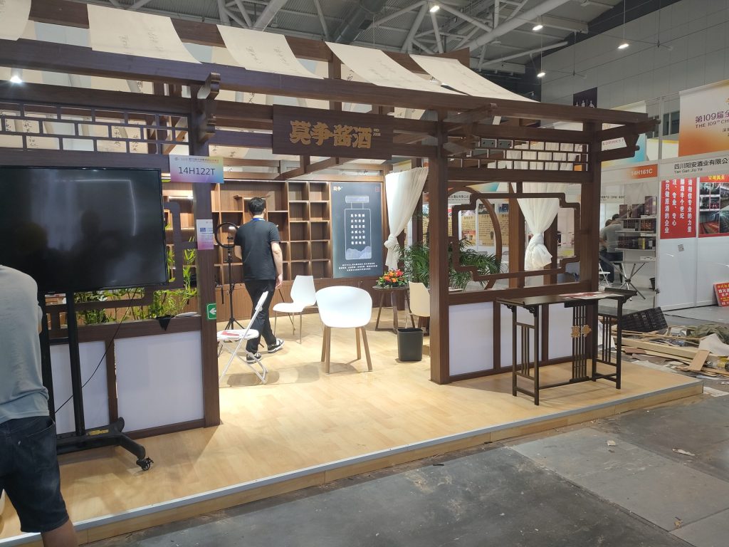 Exhibition booth with traditional East Asian wooden design, fabric roof, and a person inside, possibly during setup.