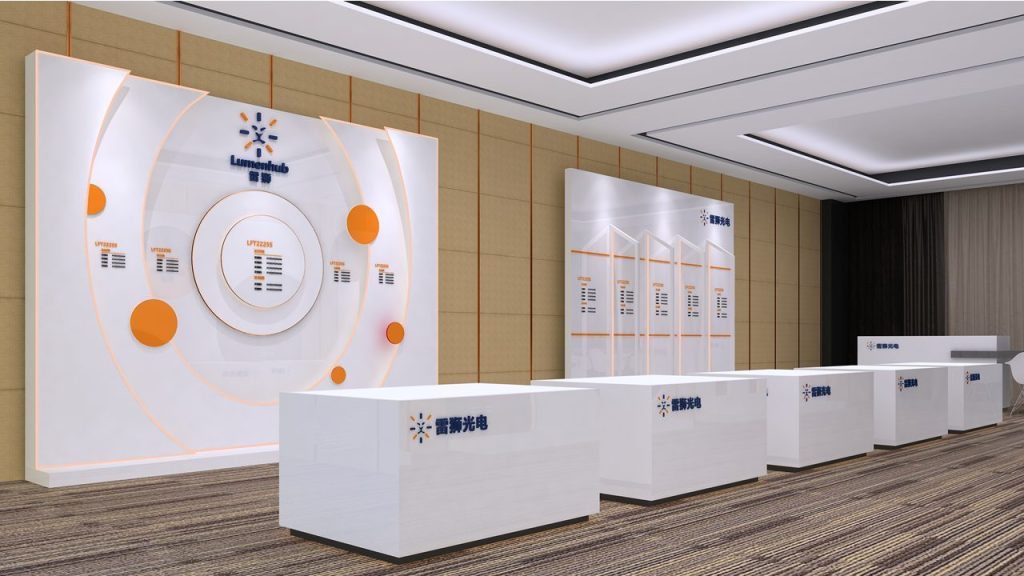 A digital rendering of a bright exhibit booth with white display counters, large white walls featuring orange circular graphics, and a patterned carpet.