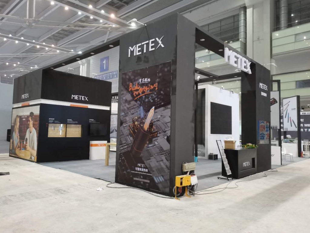 A black trade show booth in an exhibition hall, with posters showing a hand holding a glowing object and people in a cafe.