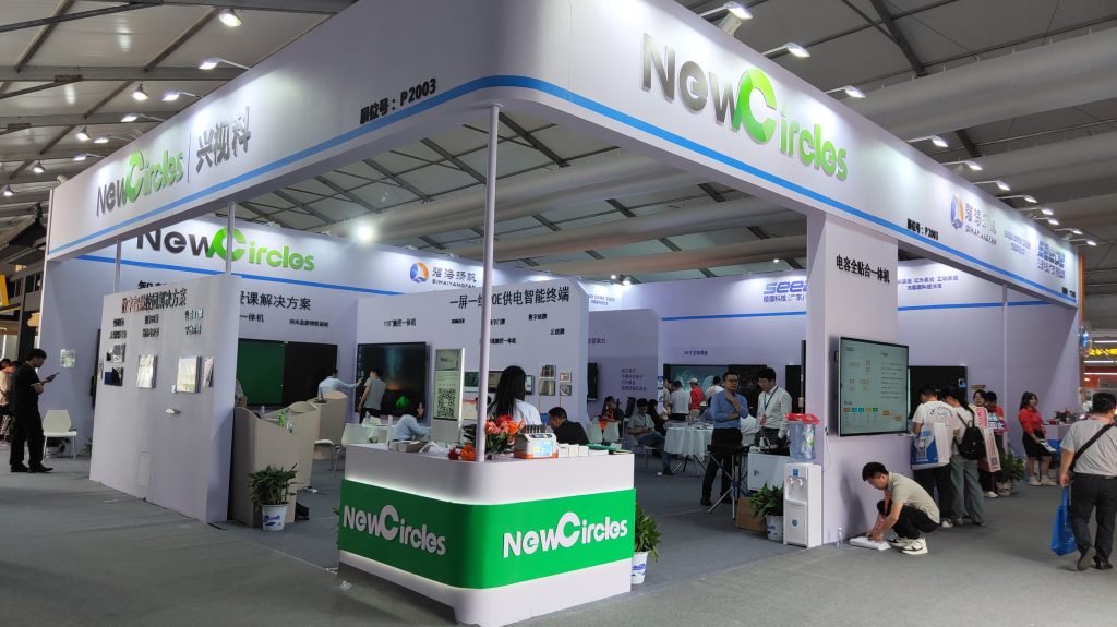 A vibrant trade show booth featuring numerous interactive displays, a service desk, and many people engaging with the exhibits in an exhibition hall.