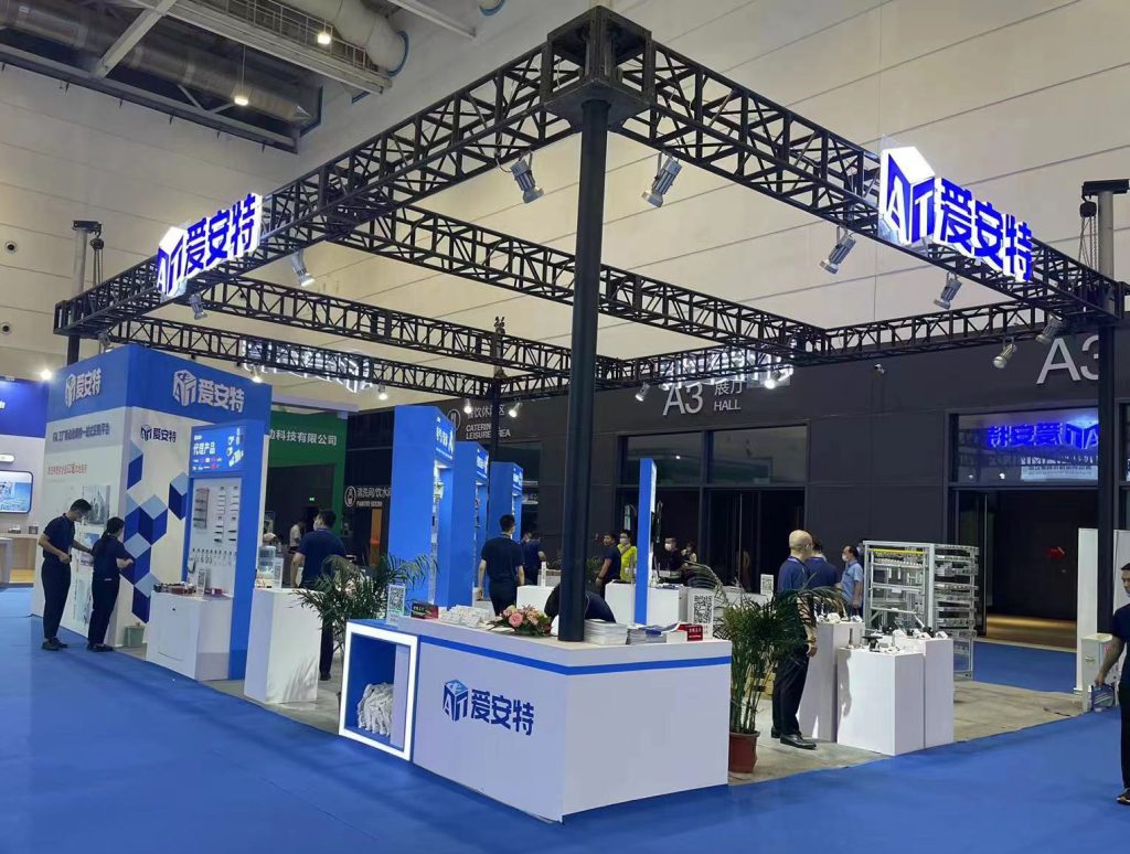 Overview of a trade show booth with blue carpet, white counters, and product displays. People are browsing the exhibits.