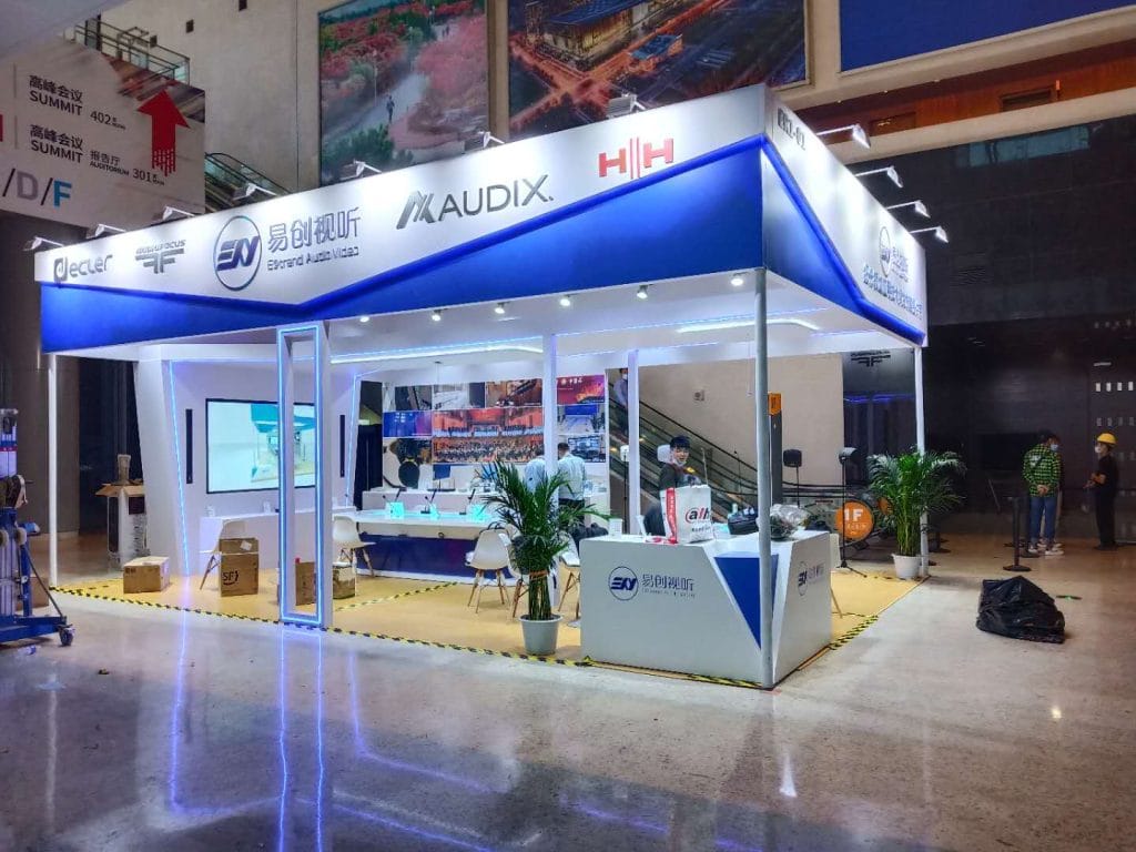 Exhibition booth with blue accents and white counters, a few people, and equipment in a convention center.