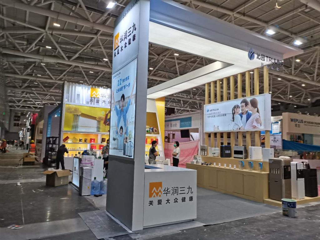 A spacious exhibition booth in a large hall, featuring multiple product displays and screens. People are casually interacting near the booth.