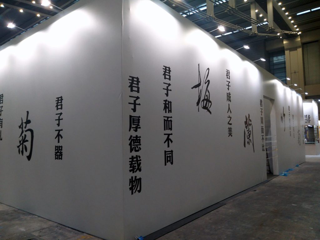 Long white exhibition wall with large black Chinese calligraphy characters, illuminated by overhead lights.