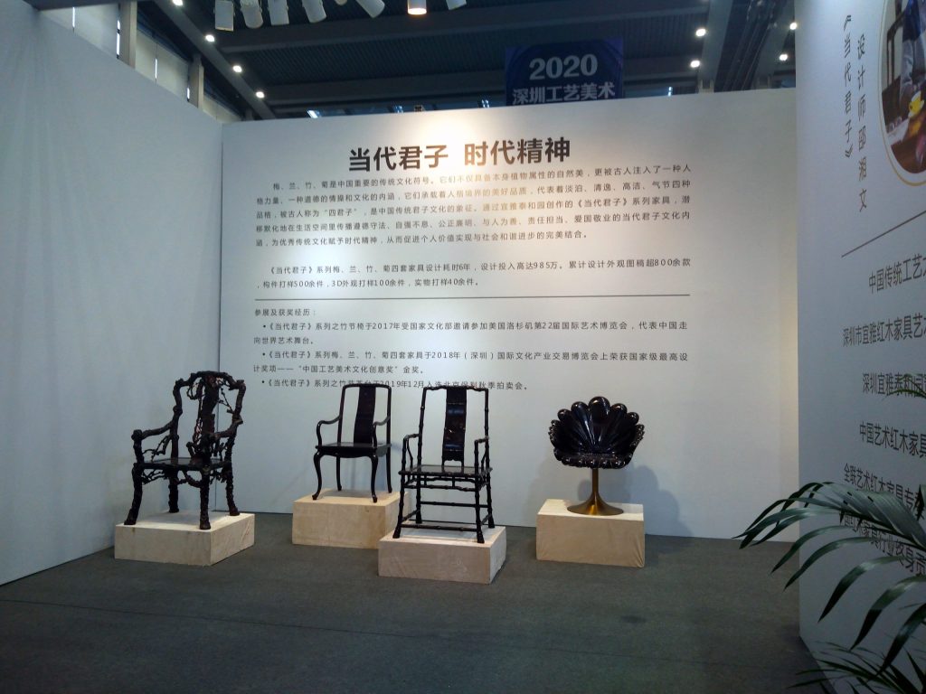 Exhibition display with a large text panel and four dark wooden chairs on individual pedestals.