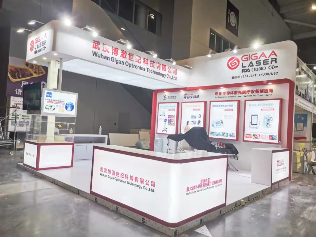 A white and red exhibition booth in a convention center, featuring multiple display panels and covered tables, preparing for an event.