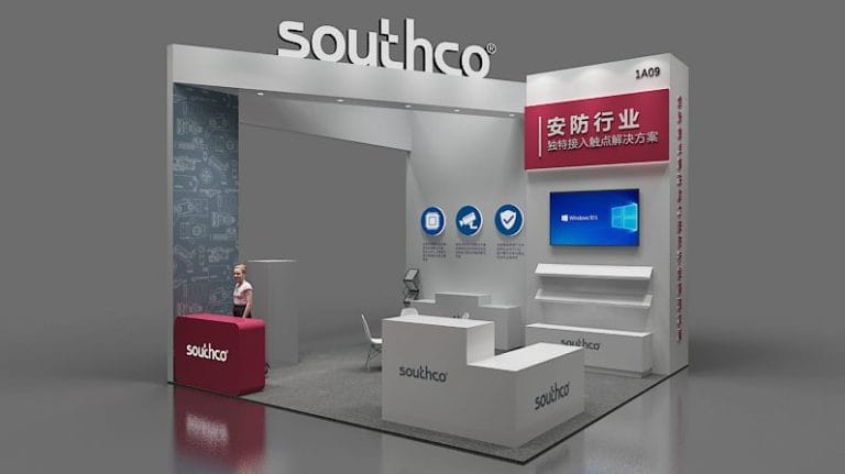 A 3D render of a modern white and red exhibition booth featuring display counters, shelves, and digital screens, with a woman behind a reception desk.